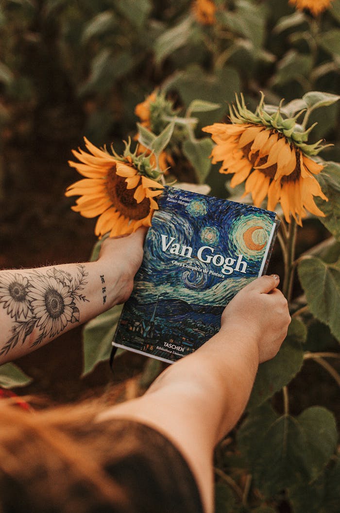 Person Holding Van Gogh Book Beside Sunflowers